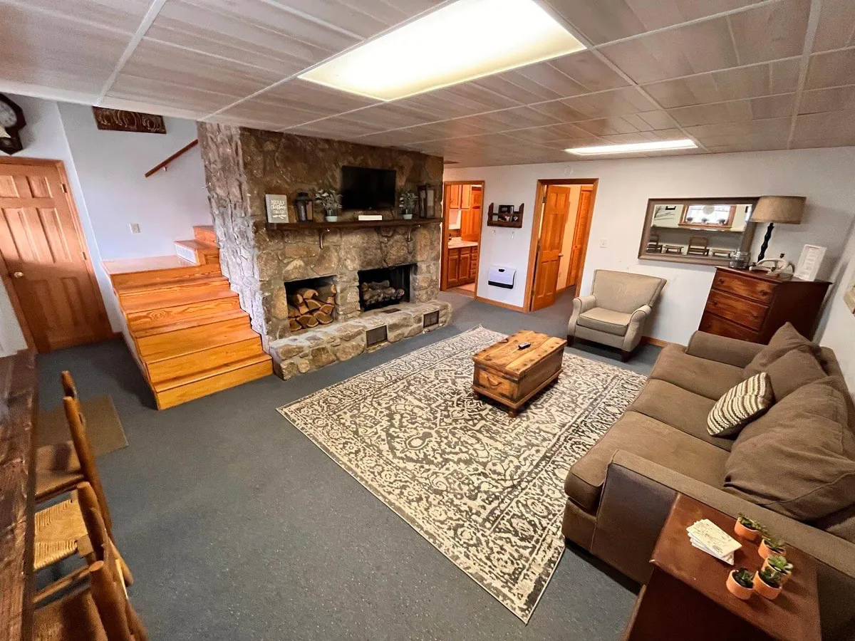 A spacious living room featuring a large stone fireplace as the focal point. Comfortable seating includes a plush sofa and a wooden coffee table, all set atop a textured area rug. The room is filled with natural light streaming in through large windows, providing a warm, inviting atmosphere ideal for relaxing or socializing.