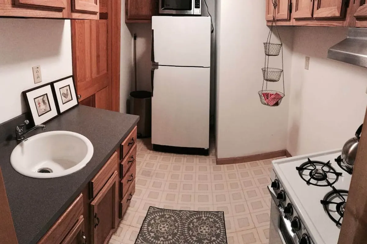 A cozy kitchen scene showcasing a sink, stove, refrigerator, a patterned kitchen rug, and wall art. The space feels homey and inviting, suggesting a welcoming environment for gathering and cooking.