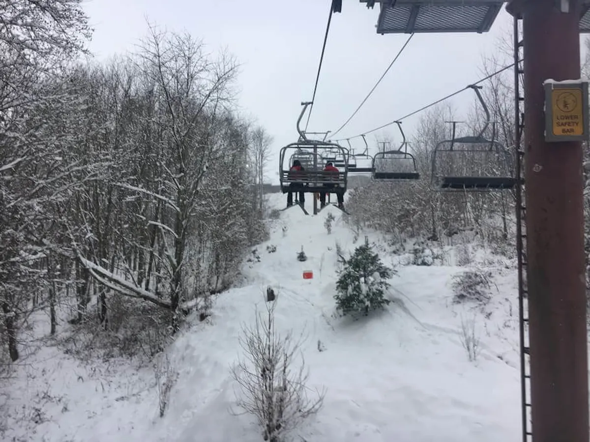 A scenic exterior view showing the ski lift ascending above snow-laden trees, with the ski slope visible beneath. The tranquil setting highlights the adventure and beauty of being right on the mountain.