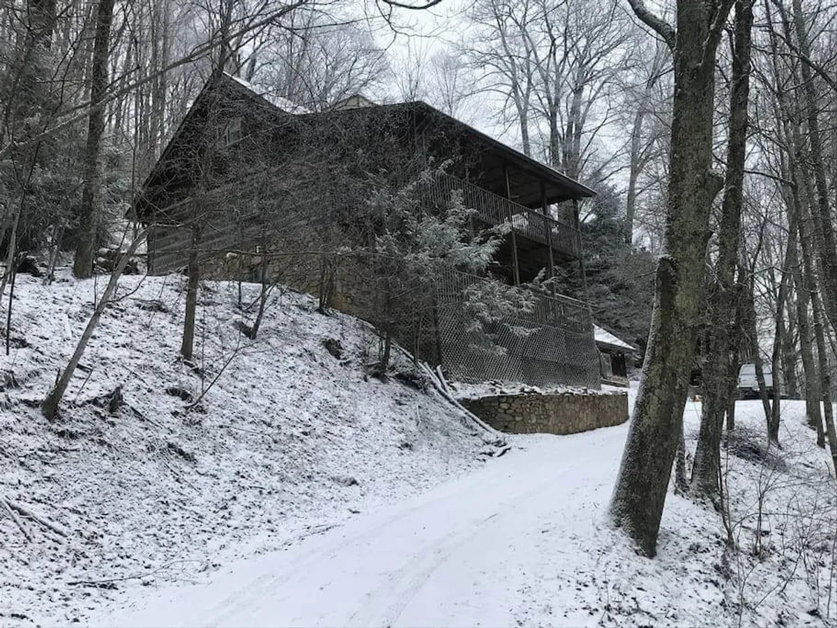 A welcoming view of the cabin’s exterior path, blanketed in snow and surrounded by tall trees. The scene emphasizes the inviting entry, the natural beauty of the landscape, and the peacefulness that comes with separation from others.