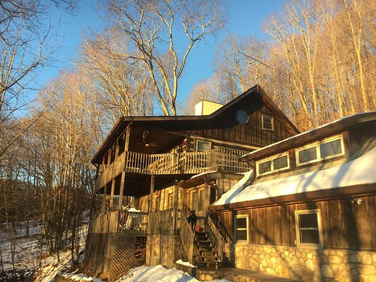 This image captures the apartment's wooden balcony with a sturdy stone foundation, nestled among tall trees and overlooking a snow-covered ground. The winter landscape sets the tone for seasonal mountain adventures and showcases direct outdoor access from the property.