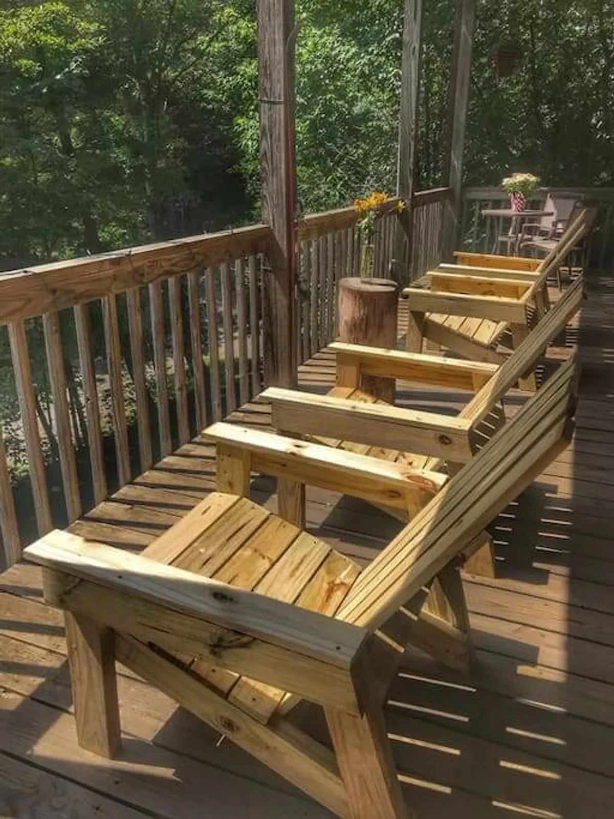 A cozy outdoor porch setup with wooden chairs, a table, and a flower vase—all basking in inviting sunlight. The porch is framed by mountain greenery, offering perfect spots for morning coffee and sunset relaxation.