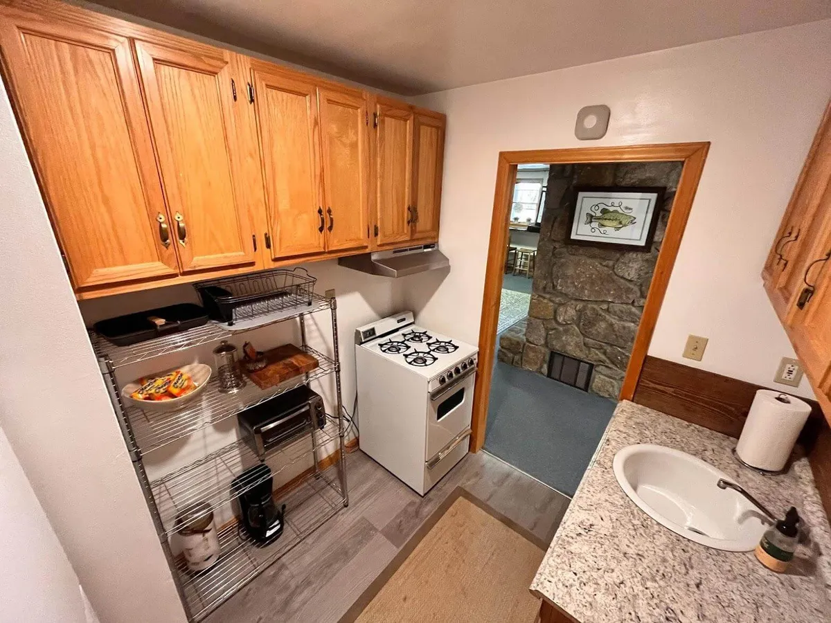 A warmly lit kitchen featuring wooden cabinets, stainless steel appliances, a granite countertop, and a kitchen island. The layout opens up towards a dining area, hinting at a seamless flow between cooking and dining spaces.